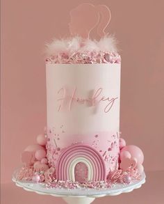 a pink and white birthday cake with a rainbow on the top, surrounded by confetti