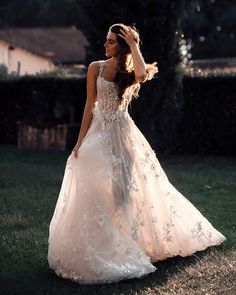 a woman in a wedding dress standing on the grass with her hands behind her head