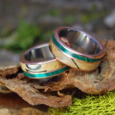 two wedding rings sitting on top of a moss covered rock next to another piece of wood