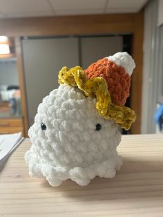 a crocheted white sheep with a yellow flower on it's head sitting on a table