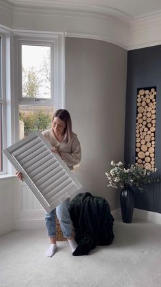 a woman holding up a piece of furniture in front of a window