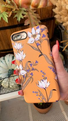 a woman's hand holding an orange phone case with flowers on it