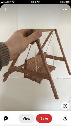 a hand is holding a miniature wooden swing