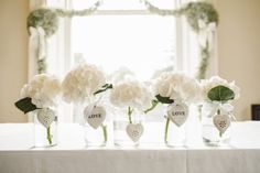 four vases filled with white flowers sitting on top of a table in front of a window