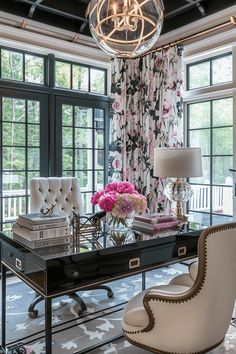 a room with a desk, chair and chandelier hanging from the ceiling in front of large windows