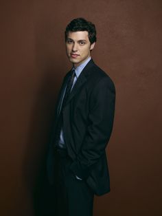 a man in a suit and tie standing against a brown wall with his hands in his pockets