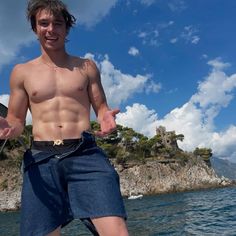 a shirtless man standing on top of a boat in the water with his hands out