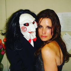 a woman standing next to a man in a creepy mask