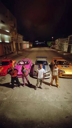 four people standing in front of three cars