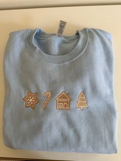 This minimalist Christmas sugar cookie crewneck is the perfect sweater to wear this holiday season. Light baby blue sweater with tan embroidered Christmas cookies. Girly Christmas embroidery, not too loud in spirit. Each Christmas cookie is shaped in holiday shaped items such as Christmas trees and candy canes. It is center chest and has white outline around the tan shapes. Unisex sizing, 50% polyester and 50% cotton. True to size, size up if you want a looser fit. Light Blue Christmas Outfit, Cookie Sweater, Butterfly Crewneck, Christmas Coal, Religious Embroidery, Embroidery Crewneck, Girly Christmas, Portrait Embroidery, Baby Blue Sweater