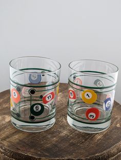 two glasses sitting on top of a wooden table filled with pool balls and billiards