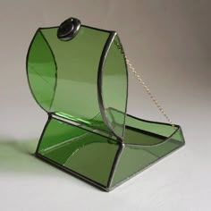 a green glass purse sitting on top of a white table next to a silver chain