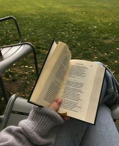 a person sitting in a chair reading a book with their legs crossed and holding an open book