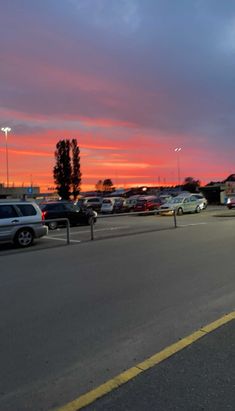 a parking lot filled with lots of parked cars under a colorful sky at sunset or dawn