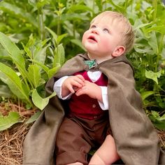 a little boy that is sitting in the grass with a blanket over his head and looking up