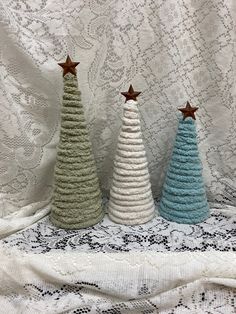 three small knitted christmas trees sitting on top of a lace tablecloth covered surface