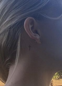 a woman with a small cross tattoo on her left side behind her ear, looking out over the ocean