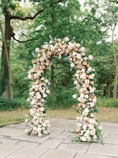 an outdoor wedding arch with flowers and greenery on the ground in front of trees