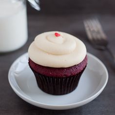 a cupcake with white frosting on a plate next to a glass of milk