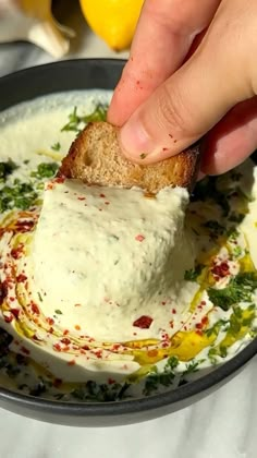 a person dipping some bread into a bowl of white sauce with lemons in the background