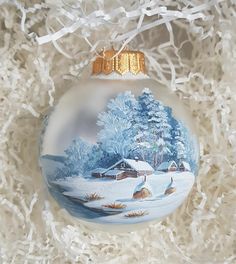 a glass ornament with a winter scene on it's side and white shredded paper in the background