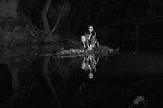 black and white photograph of a woman sitting on the edge of a body of water