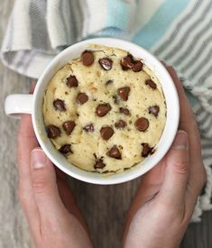 a person holding a mug with chocolate chip cookies in it