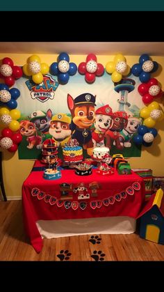 a table topped with lots of cake and balloons in front of a wall mural that has paw patrol characters on it