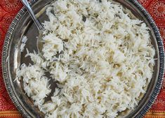 white rice in a bowl with a spoon on a red and yellow table cloth next to it