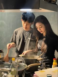 two people cooking in a kitchen with pots and pans on the stove, while one person holds a spoon