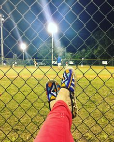 a person's feet resting on a fence with baseball field in the background at night