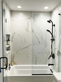 a white bath tub sitting next to a shower in a bathroom with marble walls and floors