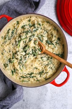 a pot filled with cheese and spinach on top of a table next to a red pan