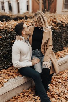 a man and woman sitting on a bench in the fall leaves