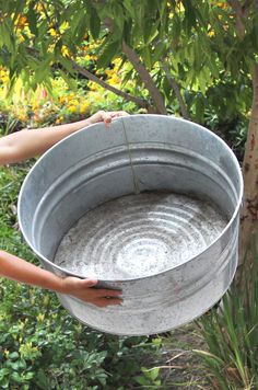 a woman is holding a metal bucket with water in it while standing next to a tree