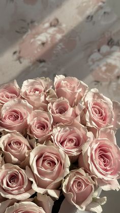 a vase filled with pink roses sitting on top of a table next to a wall