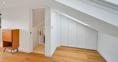 an empty room with wooden floors and white walls, along with a wood cabinet in the corner