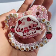 a hand holding a hello kitty brooch with beads and charms on it's wrist