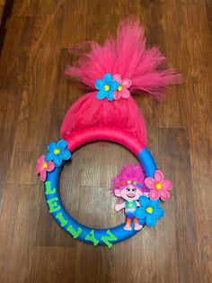 a pink and blue toy with flowers on it's head sitting on the floor