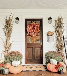 two pumpkins are sitting on the front porch next to some plants and an autumn wreath