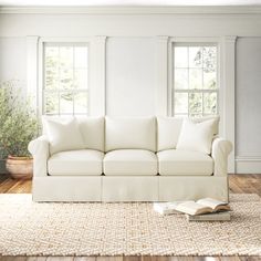 a white couch sitting on top of a hard wood floor next to two large windows