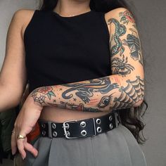 a woman with tattoos on her arm holding onto a black belt and wearing a black top