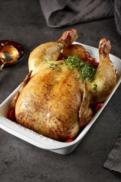 a roasted chicken in a white dish with garnish on the side and a spoon next to it