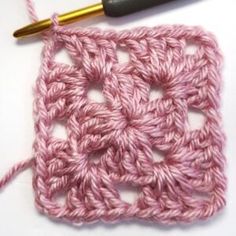 the crochet square is being worked on with a knitting needle next to it