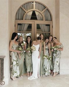 a group of women standing next to each other in front of a doorway holding bouquets