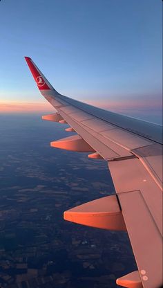 the wing of an airplane as it flies above the land and water at sunset or dawn