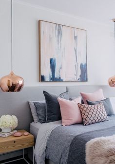 a bedroom with grey and pink bedding, white walls and artwork on the wall