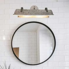 a round mirror hanging on the wall above a sink in a bathroom with white tiles