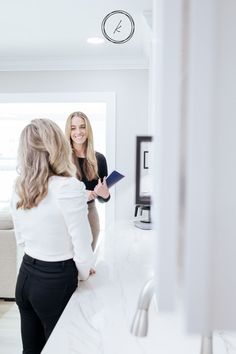 two women standing in a kitchen talking to each other and smiling at the camera woman is holding a clipboard