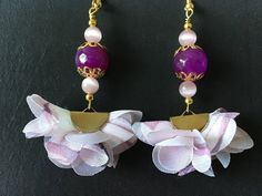 purple and white flower earrings with gold accents on a black background, hanging from golden chains